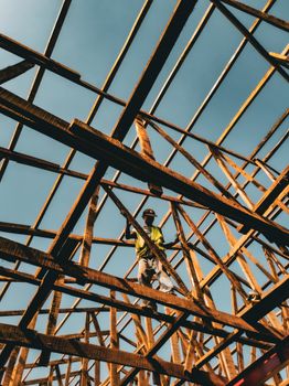 A worker balances on wooden beams at a construction site in Abuja under clear skies.