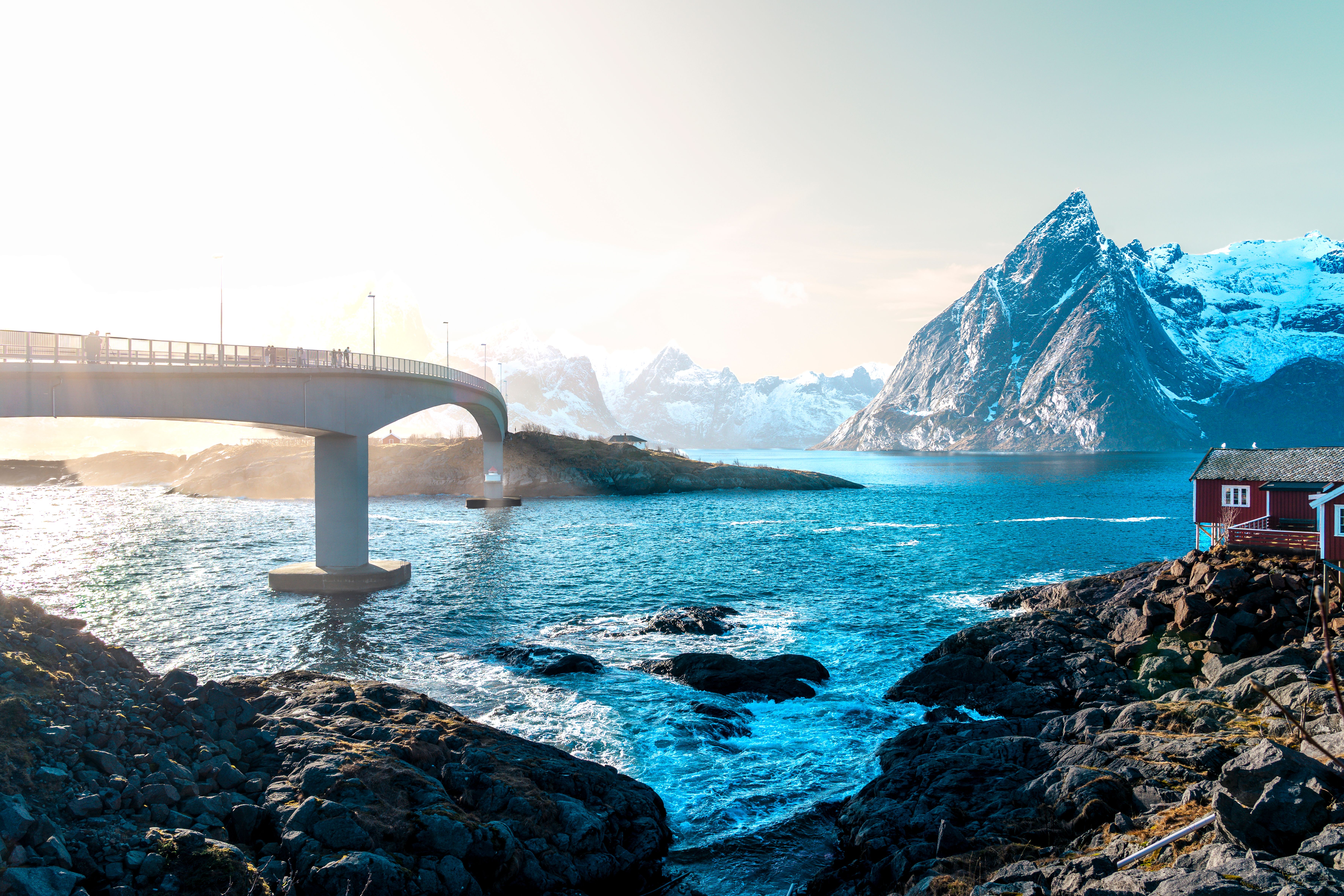 Captivating winter landscape of a bridge over turquoise waters in Lofoten, Norway with snowy mountains.
