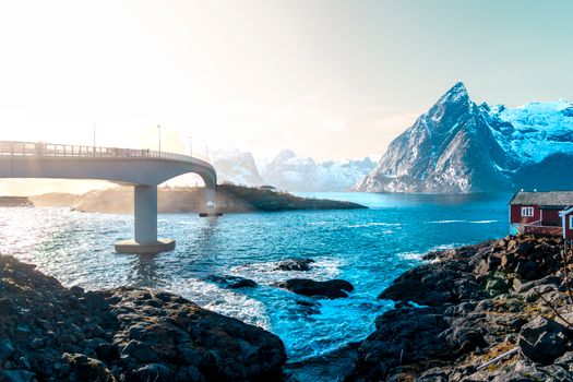 Captivating winter landscape of a bridge over turquoise waters in Lofoten, Norway with snowy mountains.