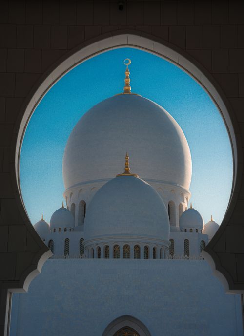 Free Stunning view of the Sheikh Zayed Grand Mosque domes framed by an arch under a clear blue sky. Stock Photo