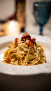 Close-up of creamy carbonara pasta topped with bacon and black pepper on a white plate.