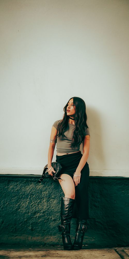 Free Elegantly dressed woman sitting against a textured wall, showcasing modern fashion and contemplative expression. Stock Photo