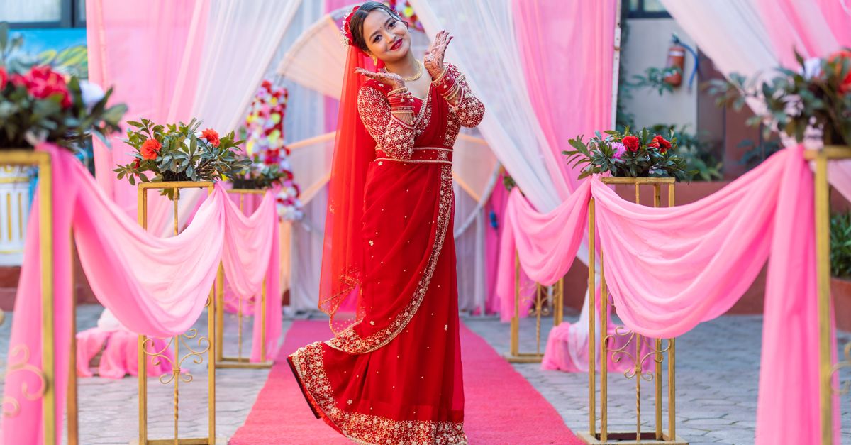 A bride in a stunning red saree poses gracefully at a beautifully decorated wedding venue.