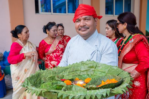 A Nepalese man in traditional attire holds a decorative leaf platter during a festival.