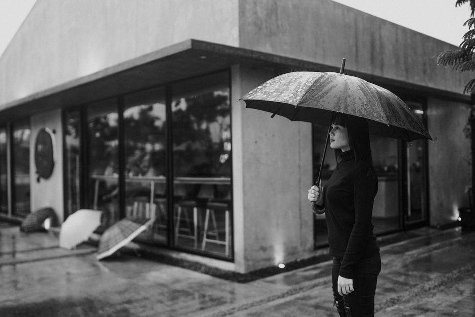 Woman holding an umbrella outside a modern building, captured in black and white.