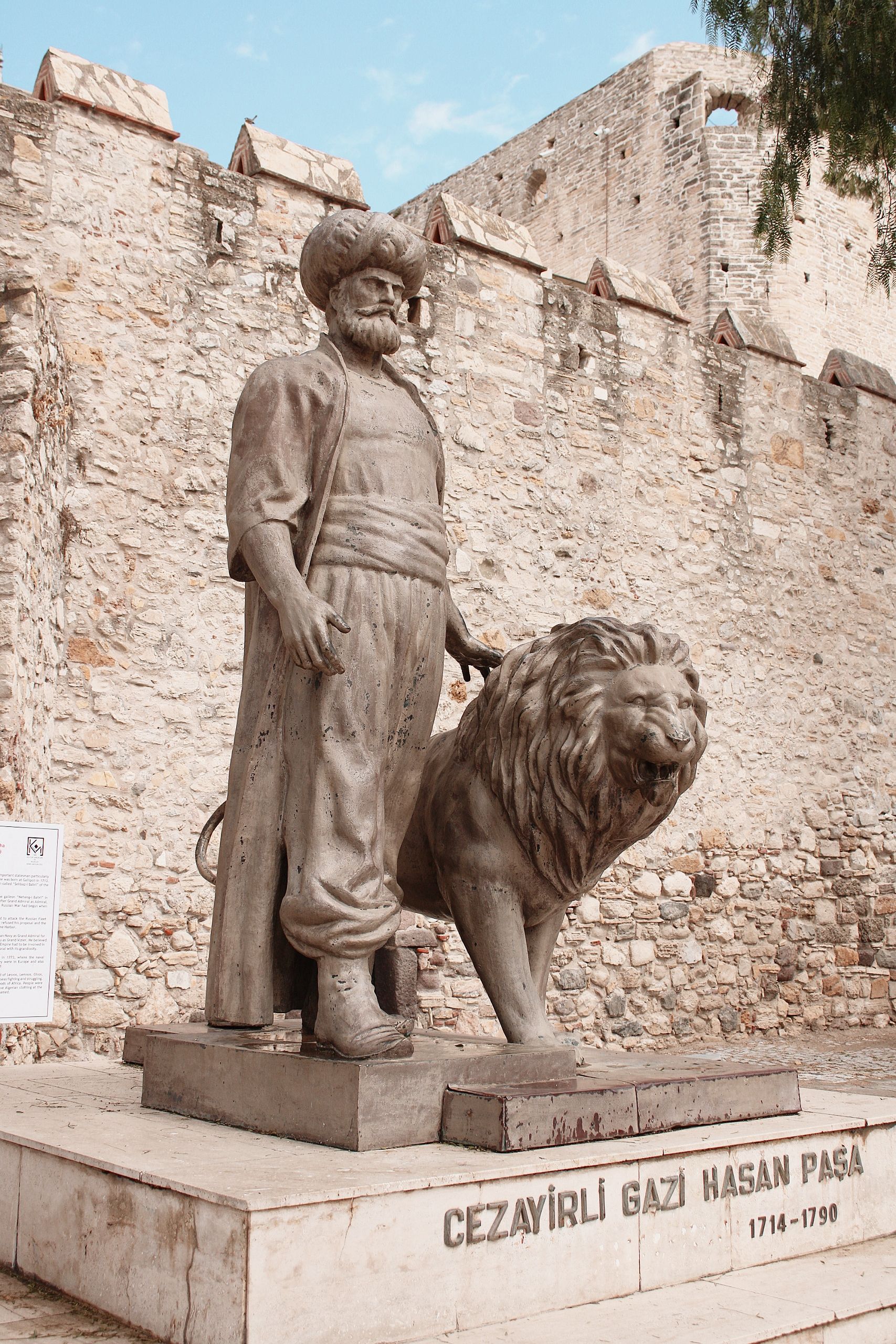 A statue of Cezayirli Gazi Hasan Pasha alongside a lion in an historical setting.