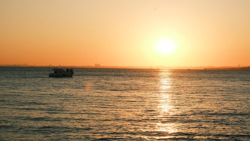 Free A peaceful sunset scene with a boat on calm ocean waters under a warm sky. Stock Photo