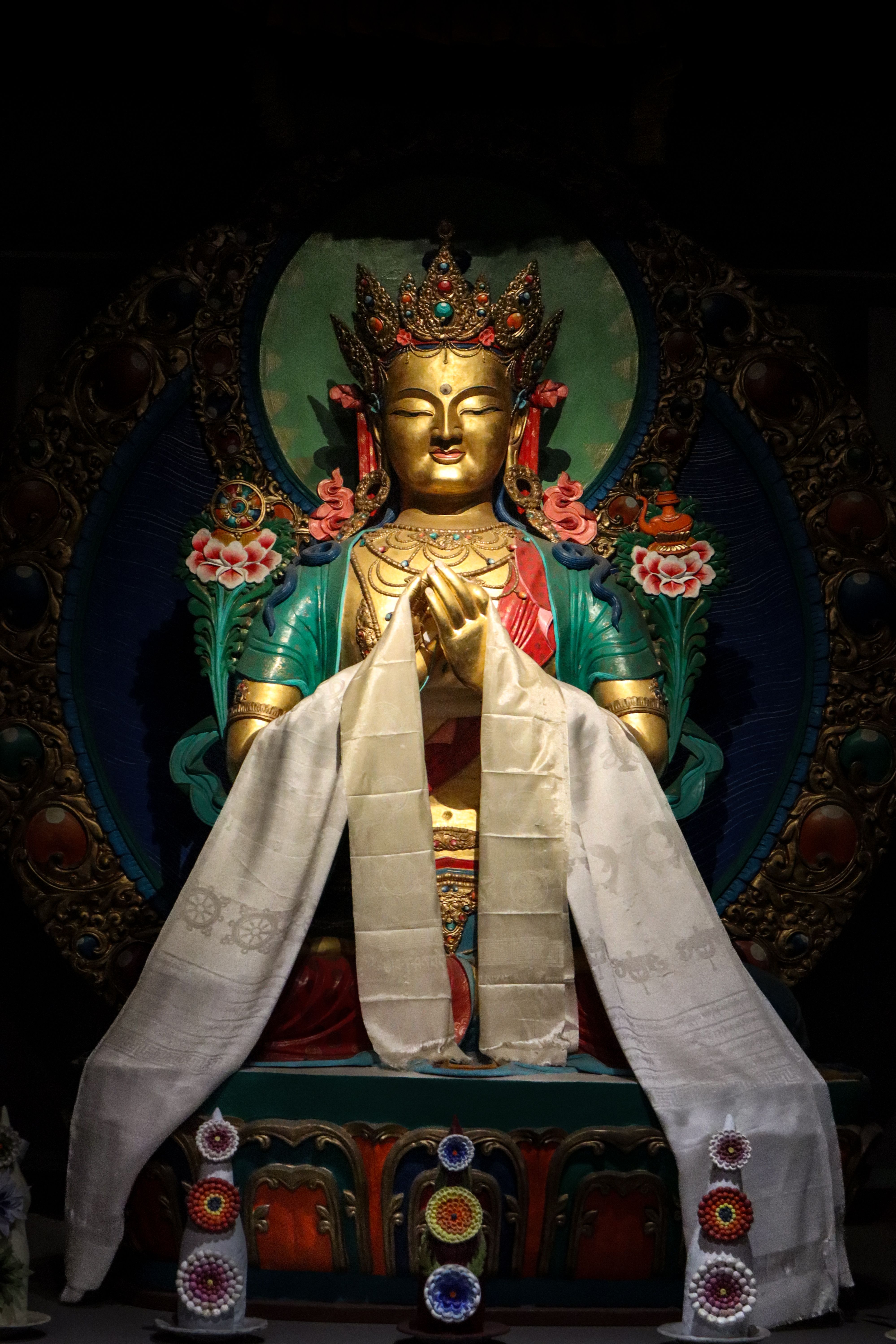 Golden Tibetan Buddha statue adorned with colorful attire in a peaceful prayer pose.