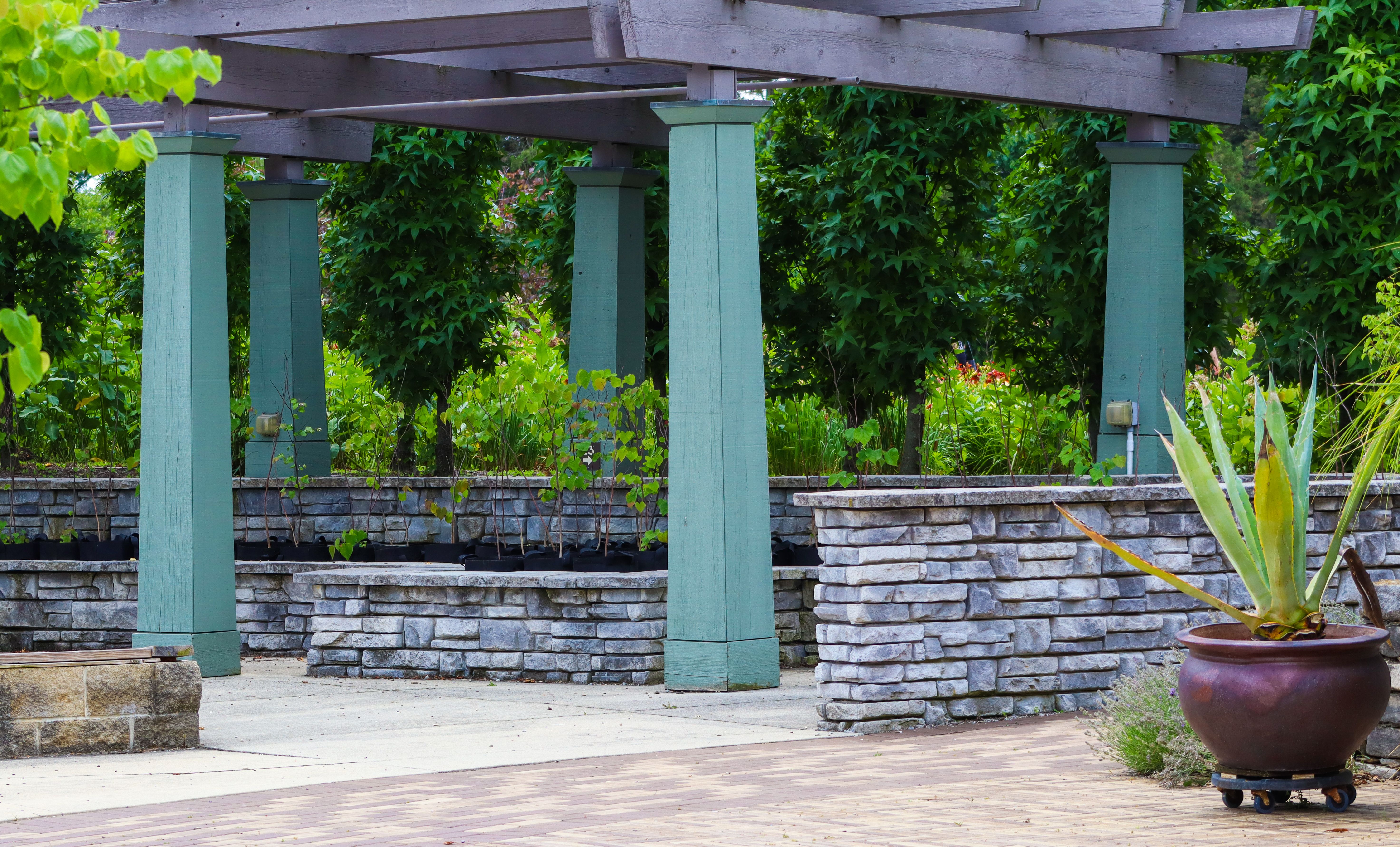 Peaceful garden setting with pergola and stone planters, featuring lush greenery.