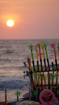 Vibrant pinwheels displayed on a beach with a stunning sunset backdrop over the ocean.