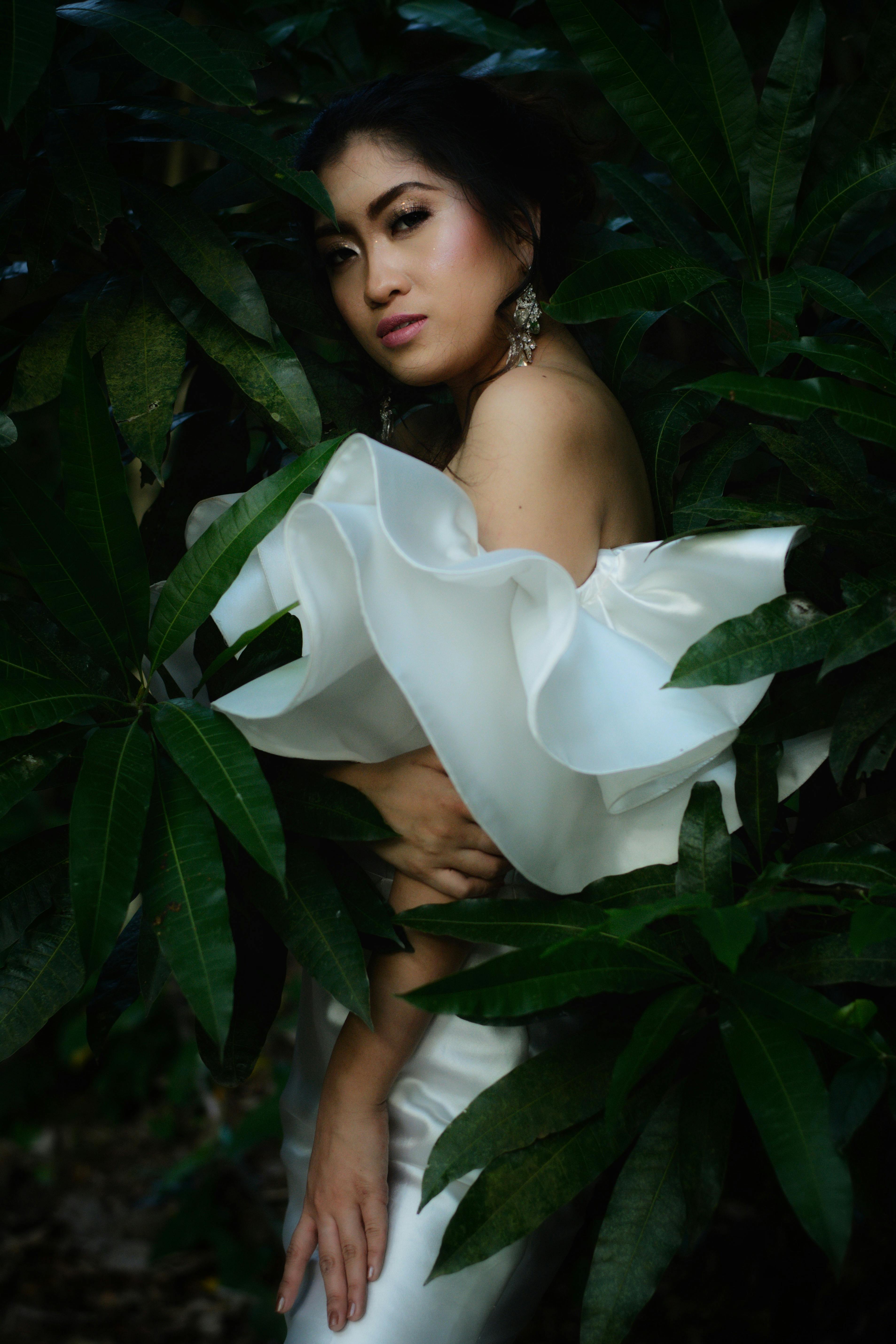 A model in a stylish white dress poses amidst lush green foliage, capturing elegance and nature.