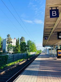 Sunlit train platform in Helsinki, Finland, featuring clear skies and lush greenery. Ideal for travel and urban themes.