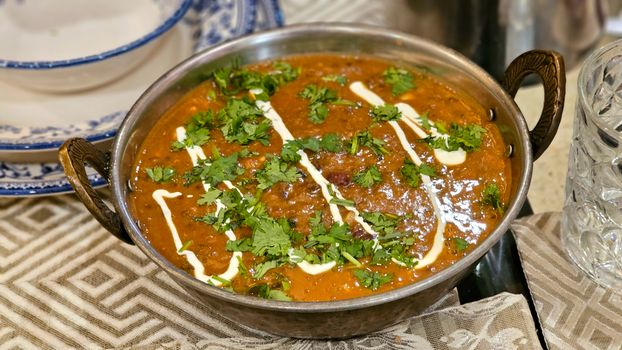 Flavorful Indian curry garnished with cilantro and cream in a traditional brass bowl.