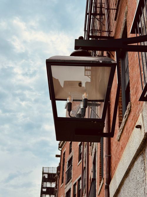 Free Vintage streetlight mounted on a brick building with blue sky backdrop. Stock Photo