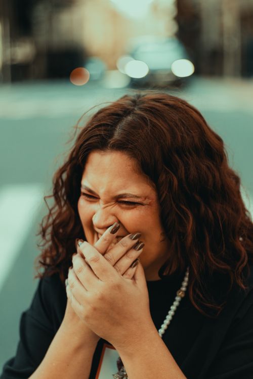 Free A happy woman laughing with hands over mouth on a city street during daytime. Stock Photo