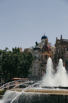 Captivating view of a classic fountain in a sunlit plaza in Valencia, Spain, showcasing historic architecture.
