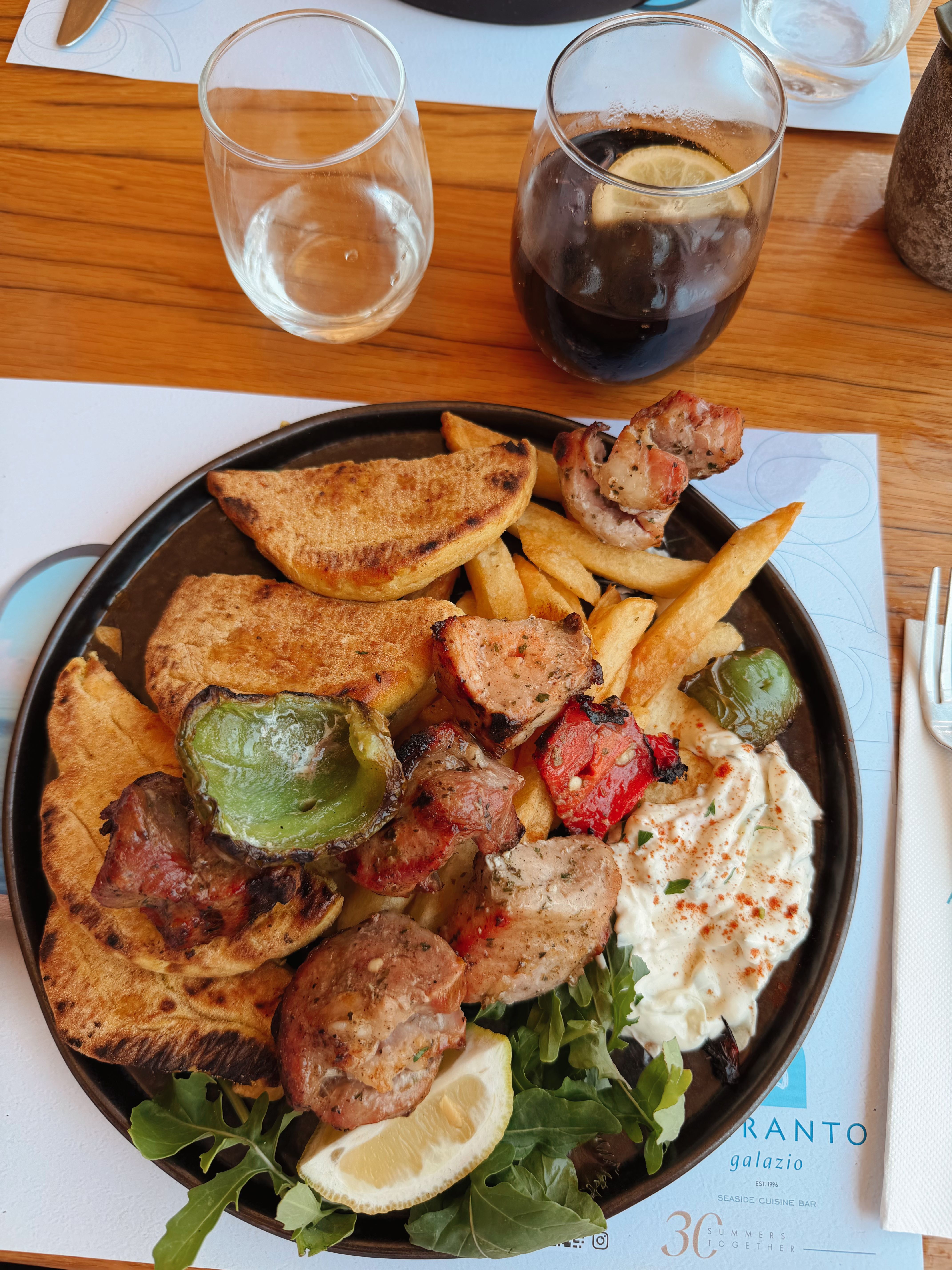 Delicious Greek souvlaki with tzatziki, served with roasted vegetables and wedges.