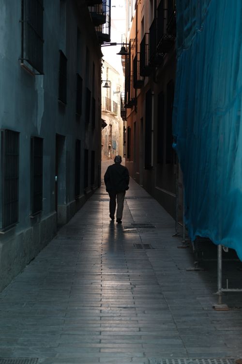 Free A solitary man walks through a narrow alley in Spain, capturing a moment of solitude and reflection. Stock Photo