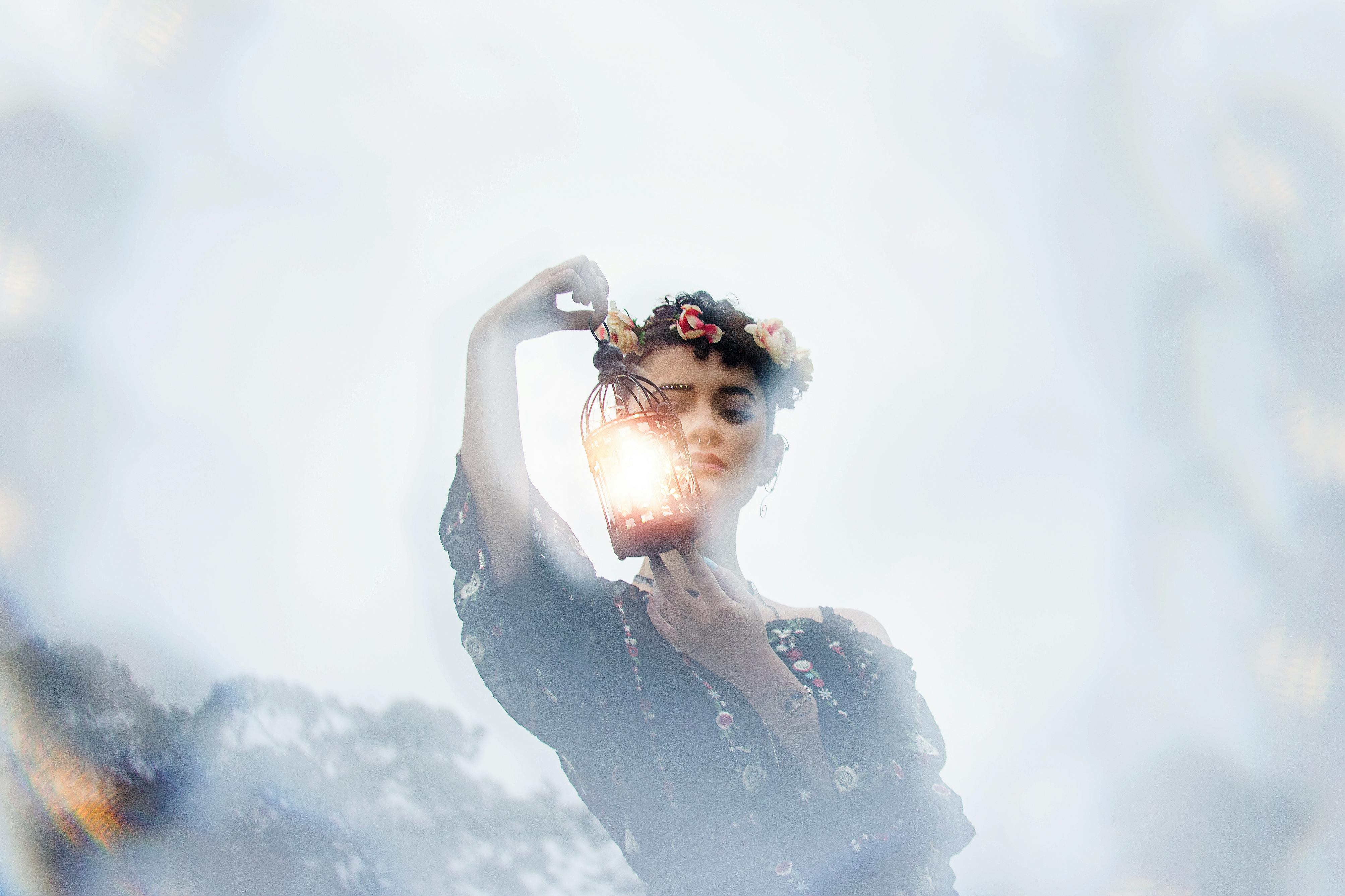 朦胧空灵的环境中，一位穿着花裙的女人手持发光的灯笼，梦幻般迷人