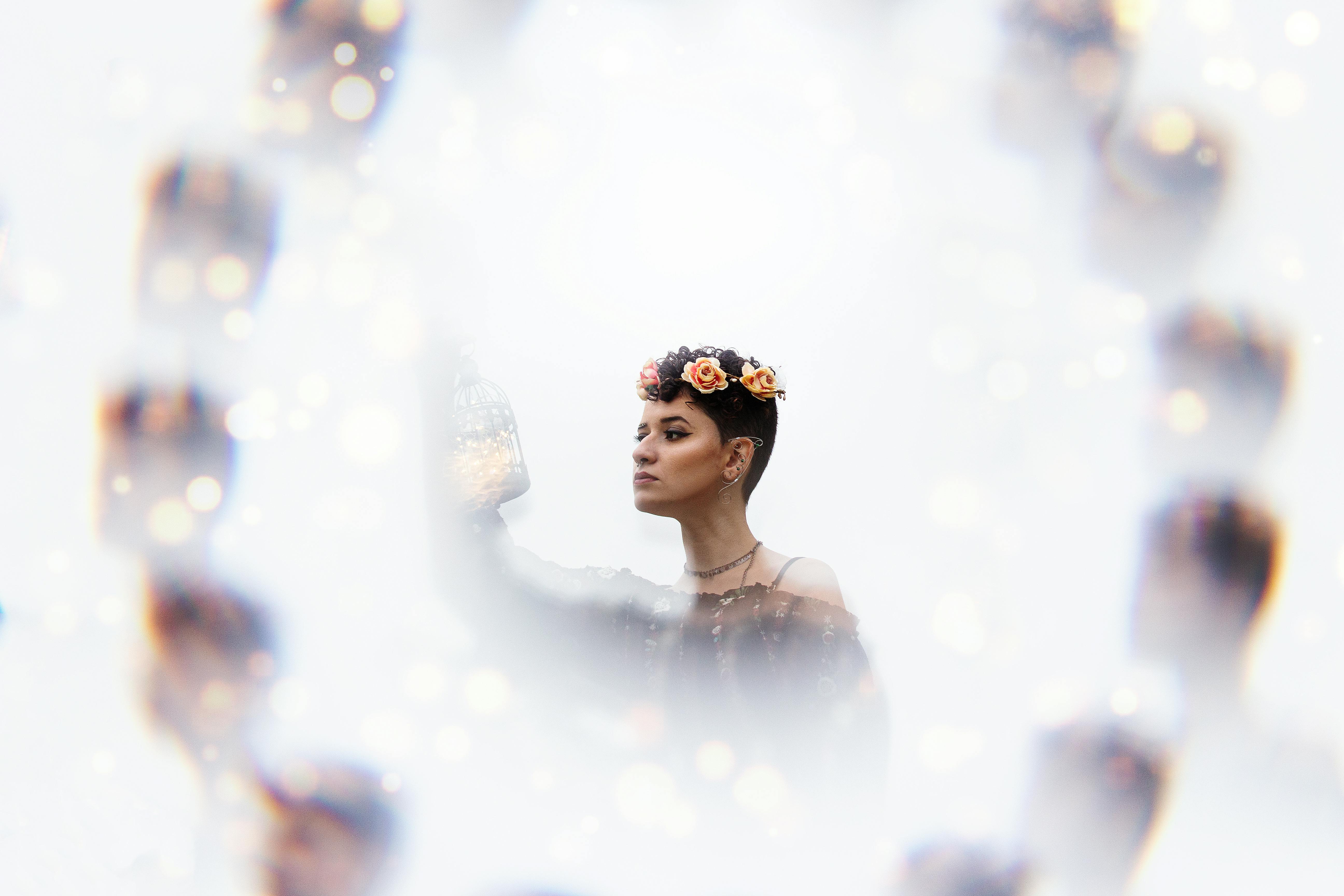 一位戴着花冠、身穿黑色连衣裙的女子手持灯笼，四周灯光闪闪发亮