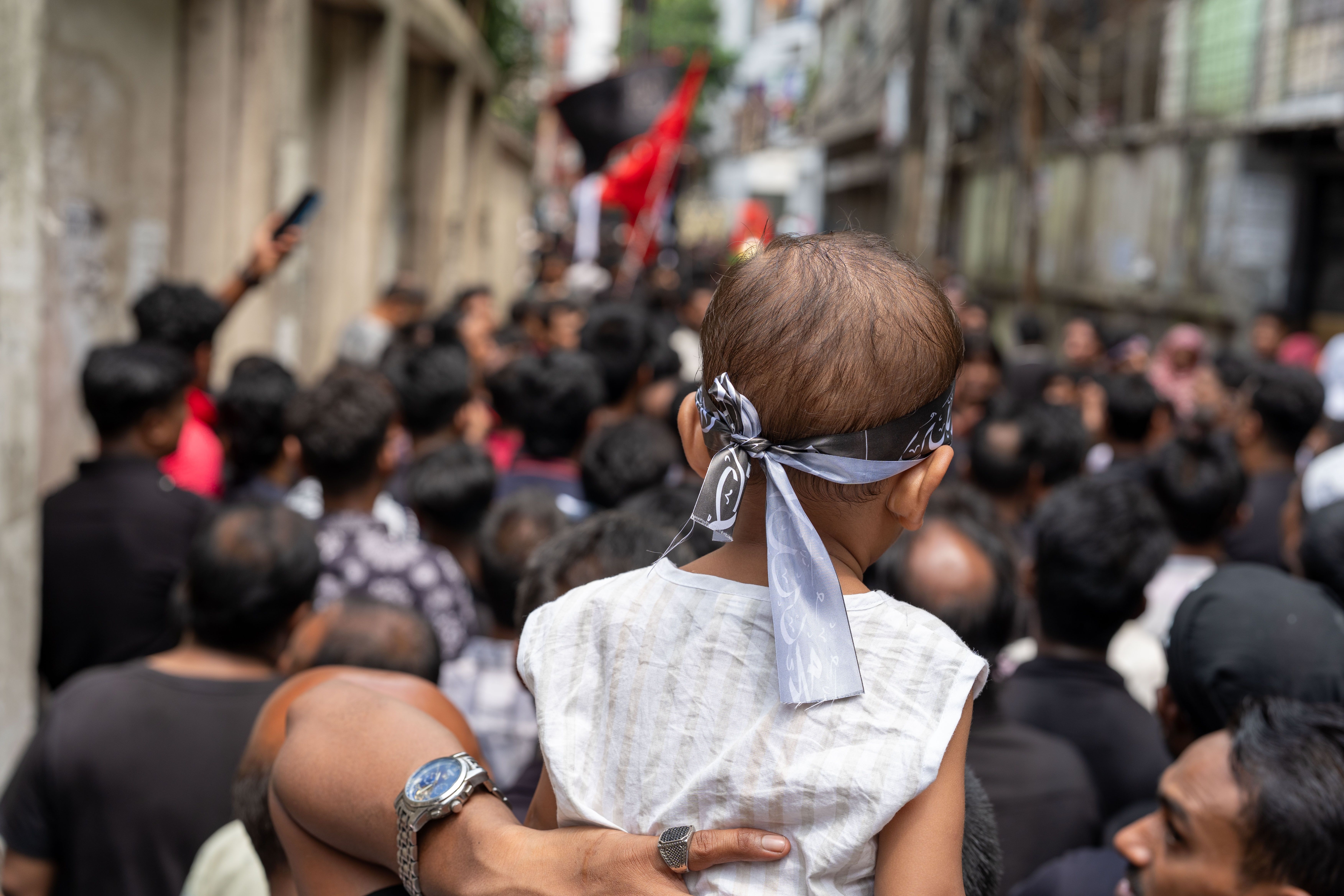 A child in a crowd, observing a street procession, showcasing cultural gathering.