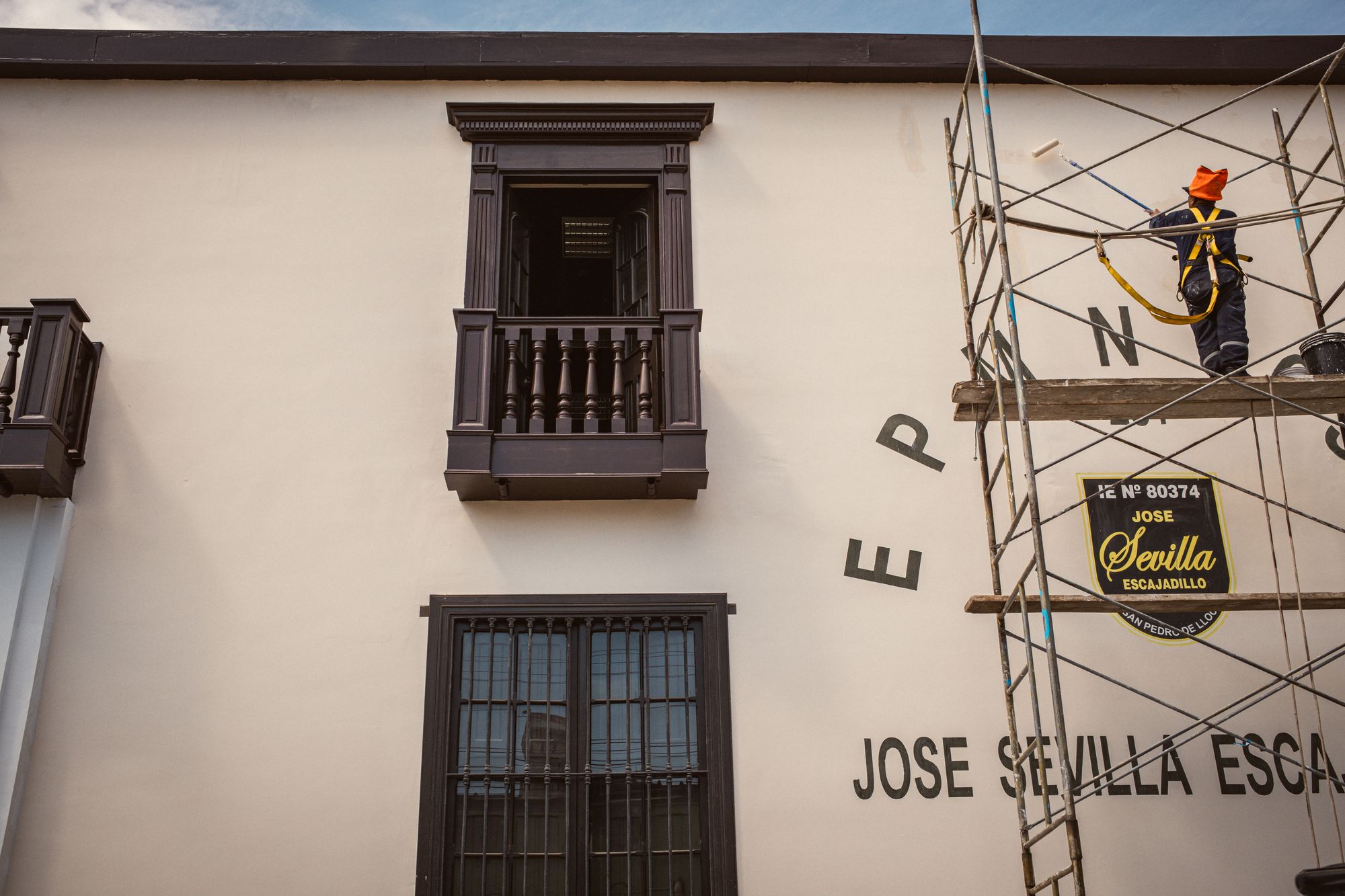 A construction worker paints a building facade while standing on scaffolding, showcasing architectural restoration.