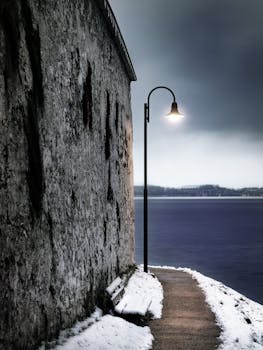 黄昏时分，一盏孤灯照亮了石墙边白雪皑皑的小路，营造出宁静的冬日景象