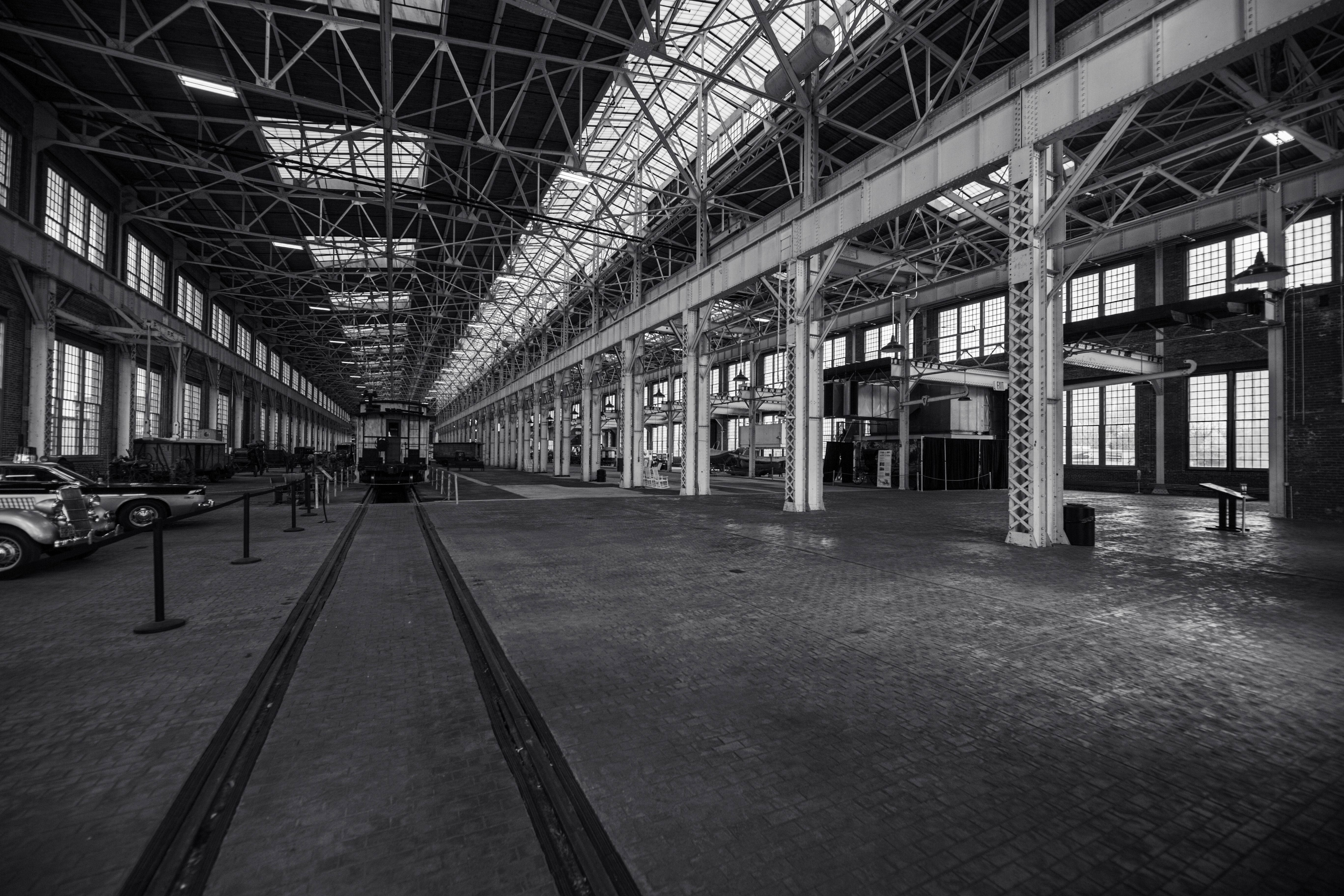 Black and white photo of an empty industrial warehouse with vintage vehicles.