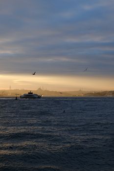 A serene sunset over Istanbul's Bosphorus, featuring a ferry on the water and silhouettes of the skyline.