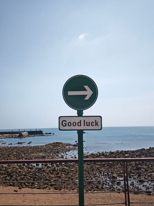 Free A seaside directional sign with an arrow and 'Good luck' message under a clear sky. Stock Photo