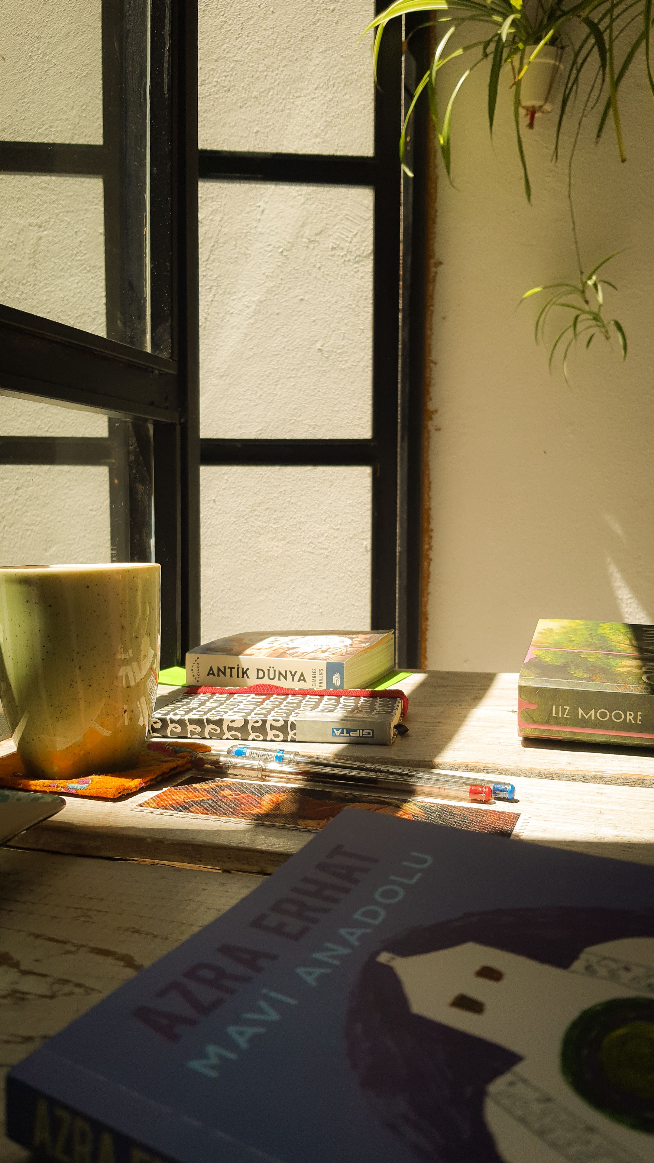 A cozy indoor reading nook with books, a mug, and sunlight filtering through a window.