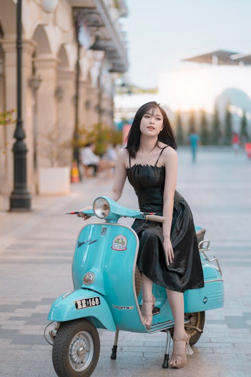 Woman In A Dress Sitting On Blue Motor Scooter