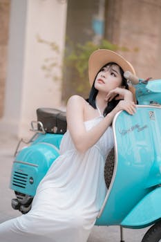 一位时尚的女人身着白色连衣裙，倚靠在绿松石色的踏板车上，在户外环境中散发着优雅