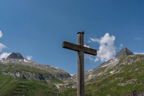 Free A wooden cross stands before majestic alpine peaks against a clear blue sky. Stock Photo
