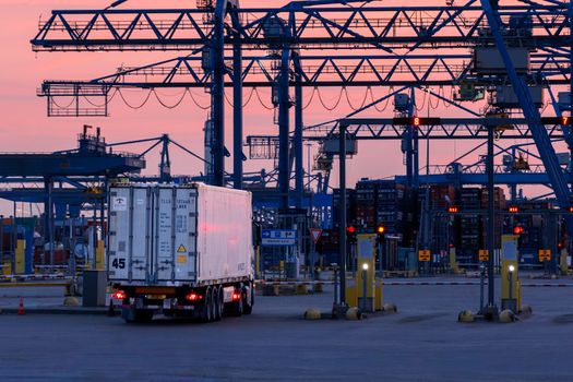 Logistics scene with cranes and a truck at Rotterdam port during sunset. Efficient cargo transportation hub.