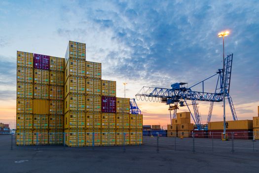 A vibrant shipping yard in Rotterdam at sunset with stacked cargo containers and cranes.