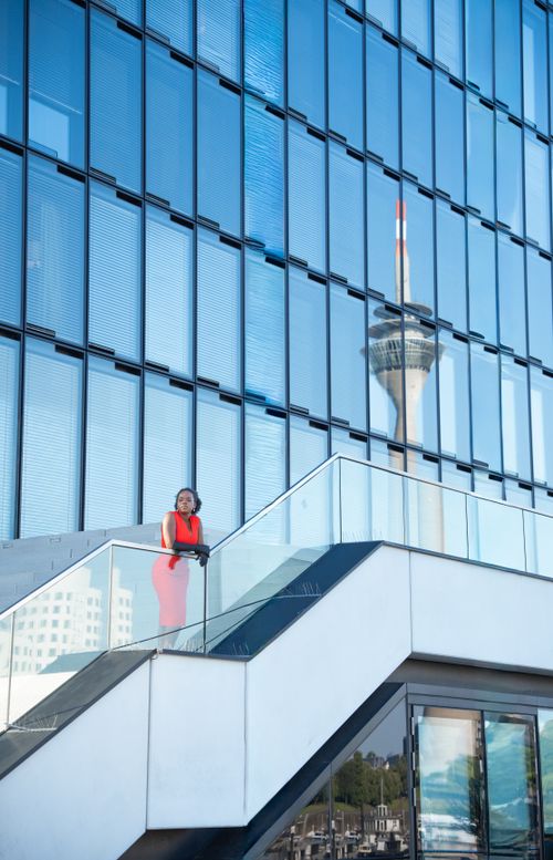 Free Woman standing on stairs with Rheinturm reflected in glass facade, Düsseldorf. Stock Photo