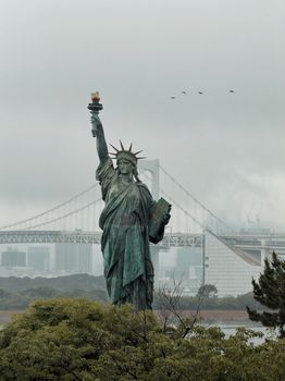 Statue of Liberty replica at Odaiba with Rainbow Bridge in Tokyo, Japan, creating a striking urban landscape.