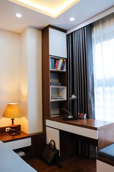 Stylish home office corner with bookshelves, desk, lamp, and curtain for a cozy work environment.