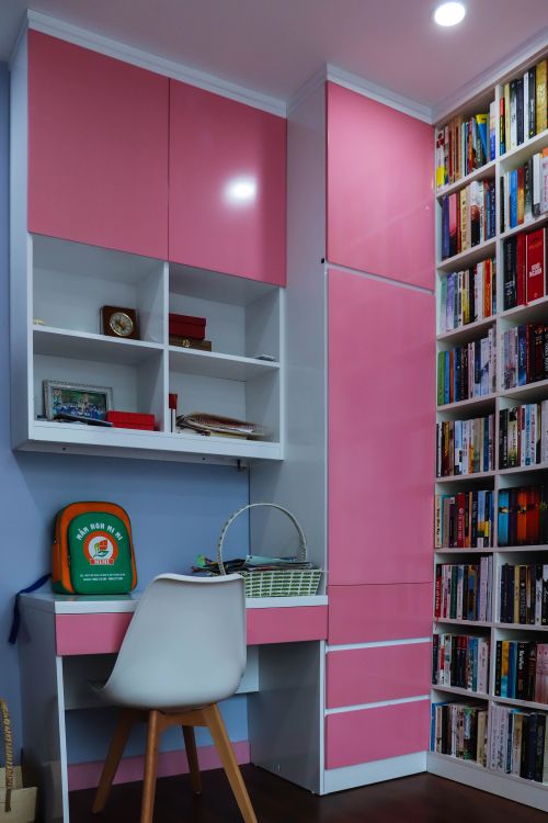 Free Vibrant home office setup with pink cabinets, a desk, and a filled bookshelf. Stock Photo