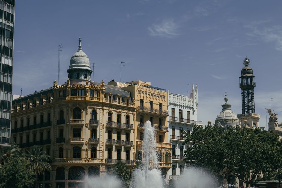 Encantador paisaje urbano de Valencia con edificios históricos y una fuente animada en un día soleado.