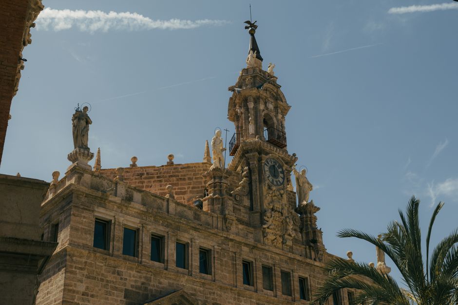 Acercamiento de una torre del reloj histórico con esculturas en Valencia bajo un cielo azul.