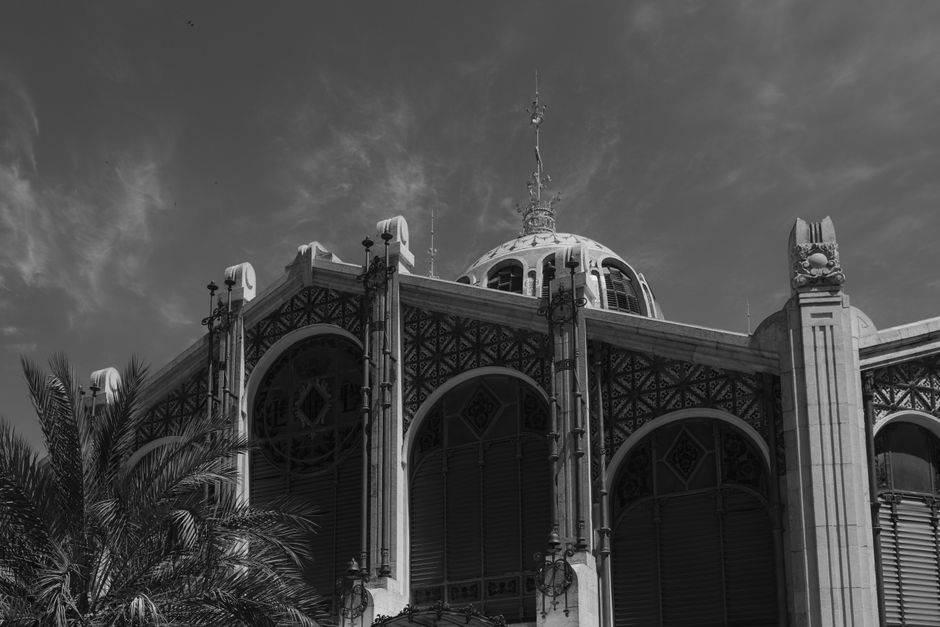 Fotografía en blanco y negro del Mercado Central de Valencia, que muestra su intrincada arquitectura contra un cielo nublado.