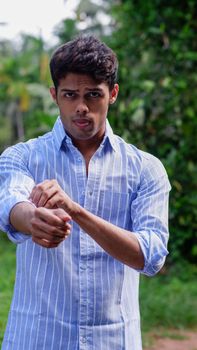 Confident young man with serious expression adjusting his sleeves in a natural outdoor setting.