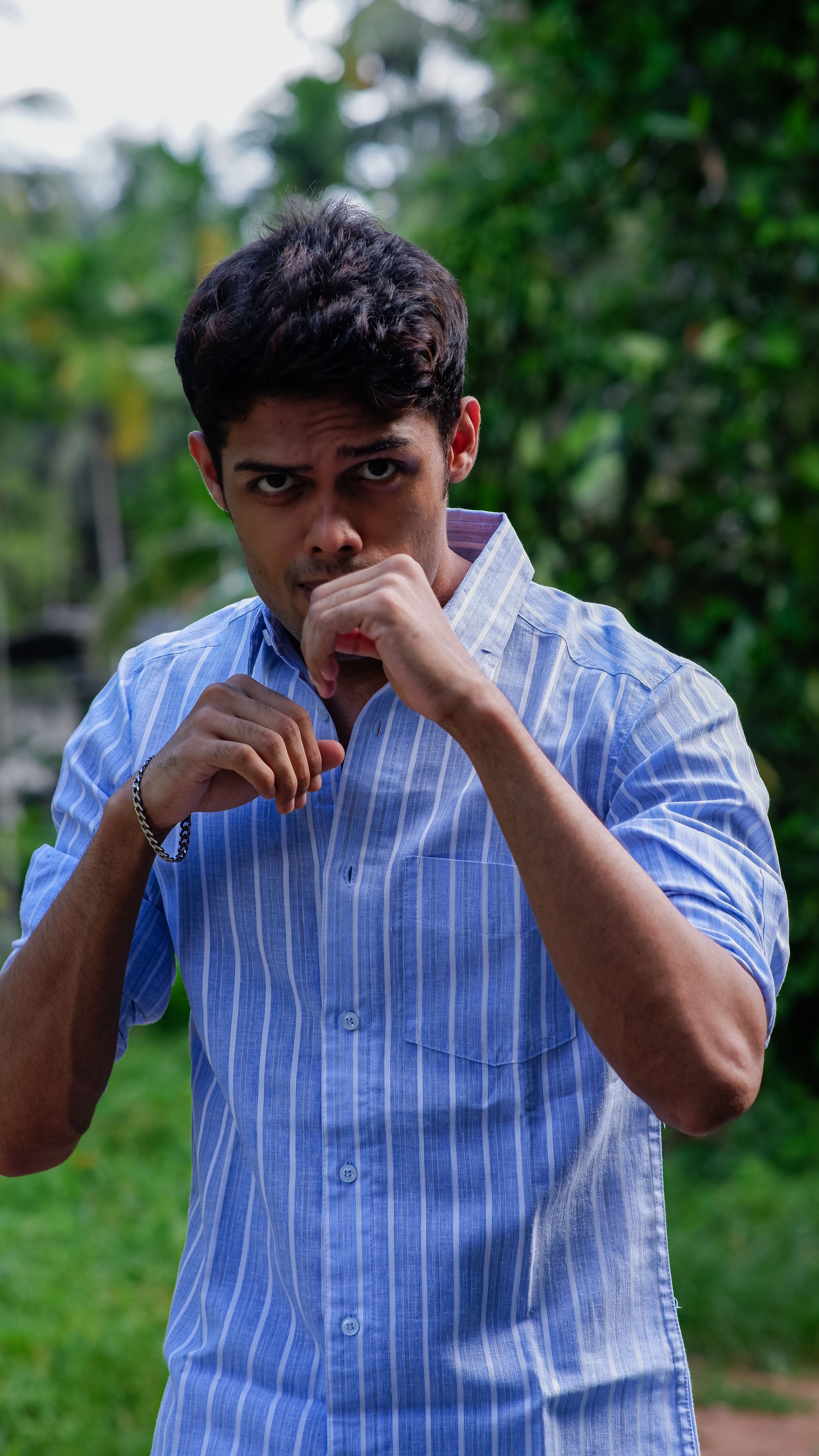 Portrait of a young man in a striped blue shirt standing outdoors posing with confidence.