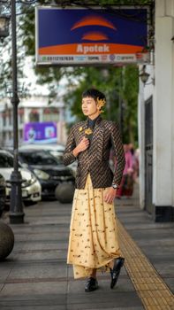 Man in traditional Indonesian attire walking on a busy street in Bandung, showcasing local fashion. - Fotografer Sidoarjo