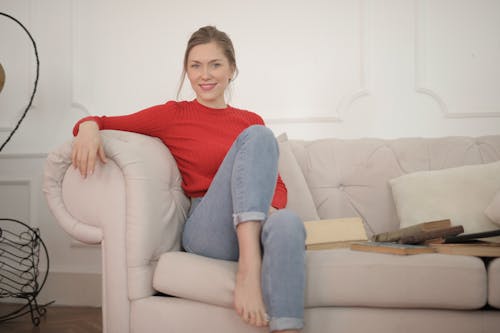 Free Woman In Red Long Sleeved Shirt And Blue Denim Jeans Sitting On Couch Stock Photo