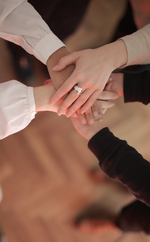 Top view of faceless friends in different clothes stacking hands together while standing on wooden floor indoor on sunny day