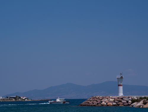 Free Lighthouse on Izmir coast with a boat passing by on a bright summer day. Stock Photo