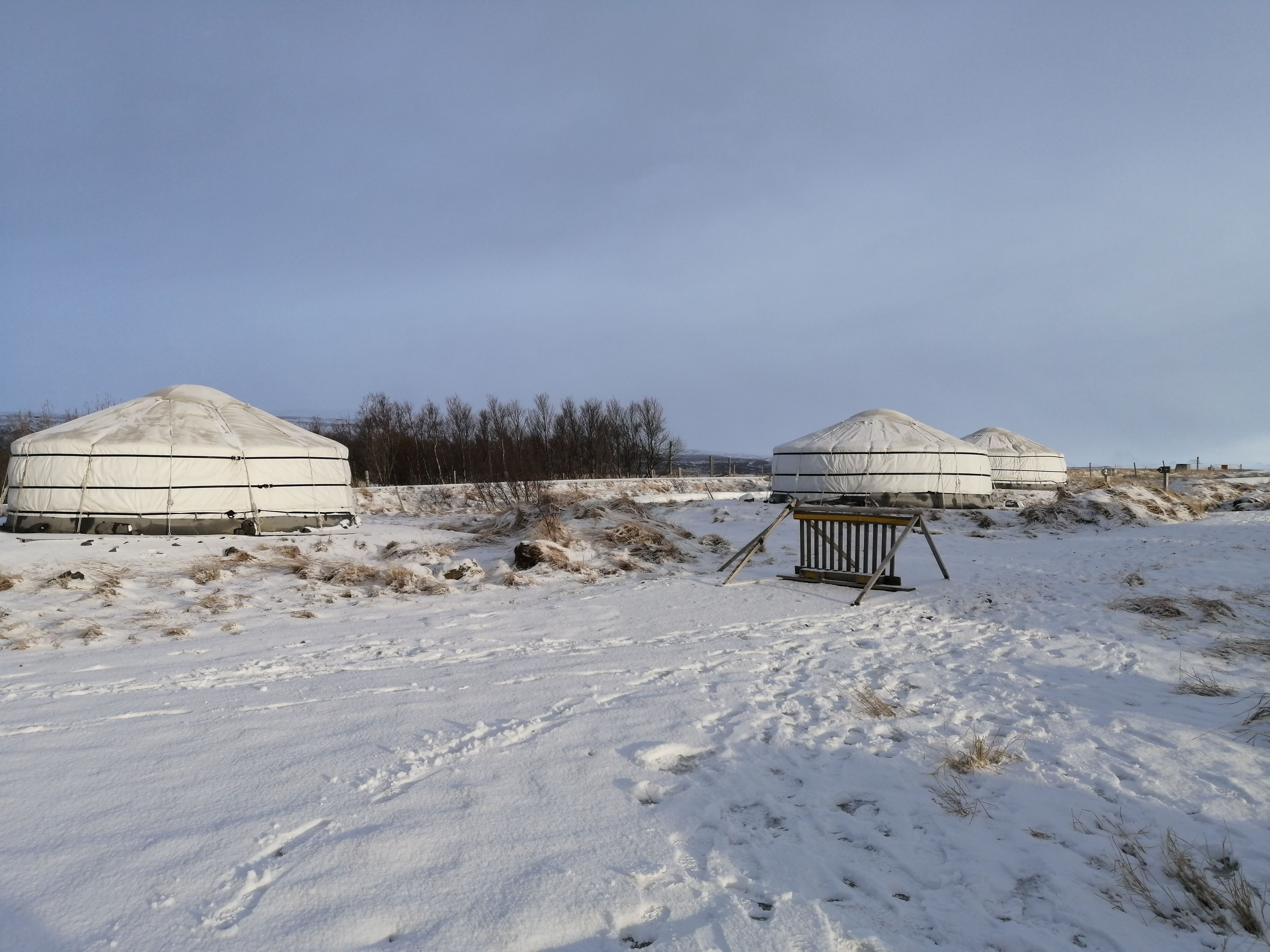 Snow-covered landscape with traditional yurts under a clear winter sky, serene and remote.